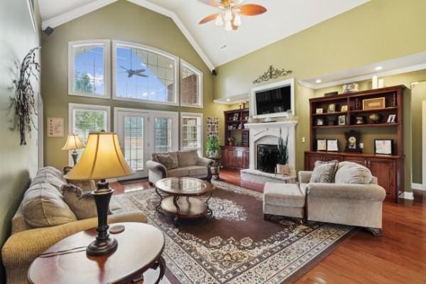 living area with a ceiling fan, wood finished floors, high vaulted ceiling, and a fireplace with raised hearth