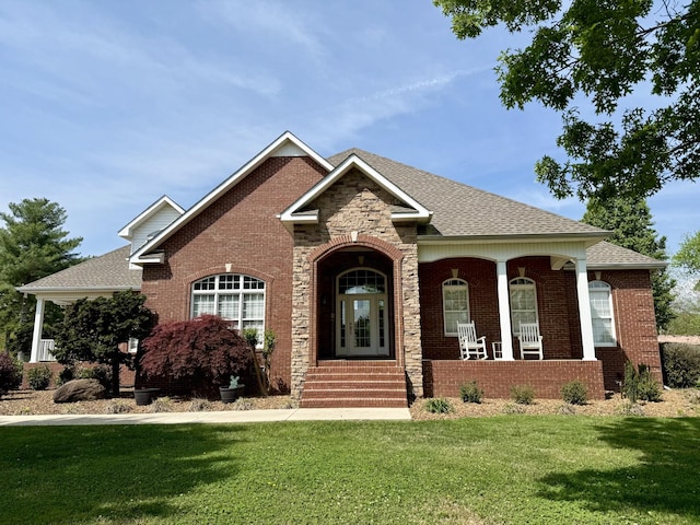 craftsman house with a porch, roof with shingles, a front yard, and brick siding