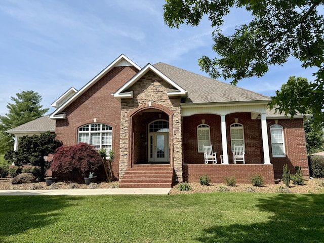 view of front of house with brick siding, a porch, a shingled roof, and a front yard