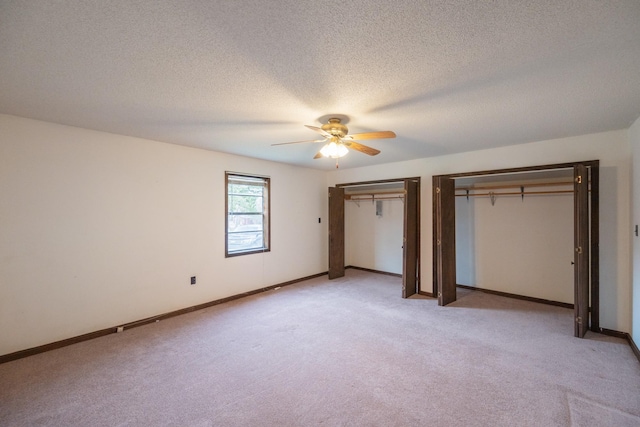 unfurnished bedroom featuring two closets, baseboards, light colored carpet, a textured ceiling, and a ceiling fan