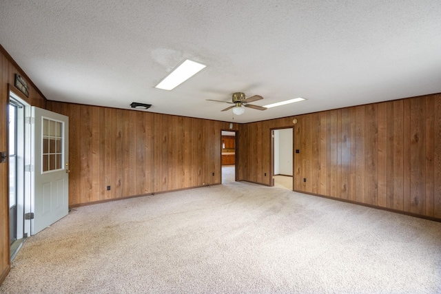 unfurnished room featuring light carpet, wooden walls, a textured ceiling, and a ceiling fan
