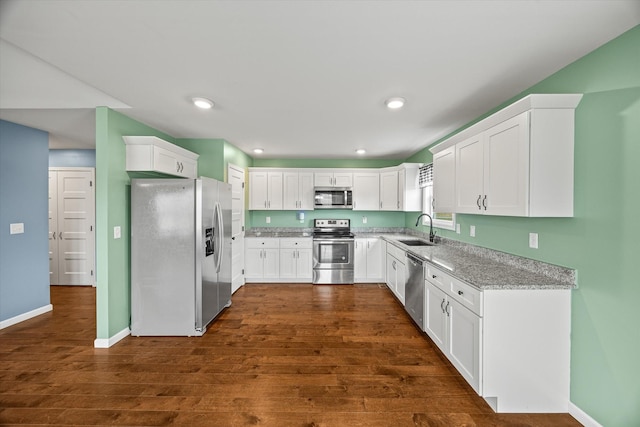 kitchen with a sink, dark wood-style floors, white cabinetry, appliances with stainless steel finishes, and light stone countertops