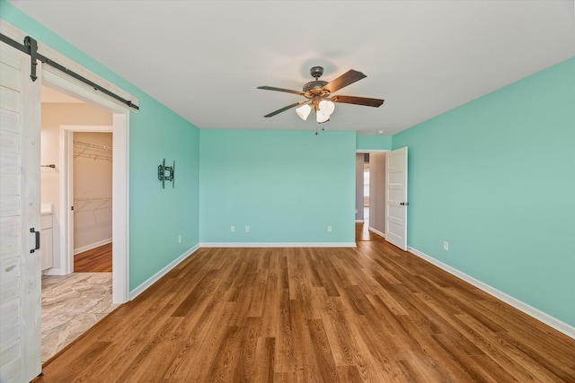 empty room featuring baseboards, a ceiling fan, a barn door, and wood finished floors