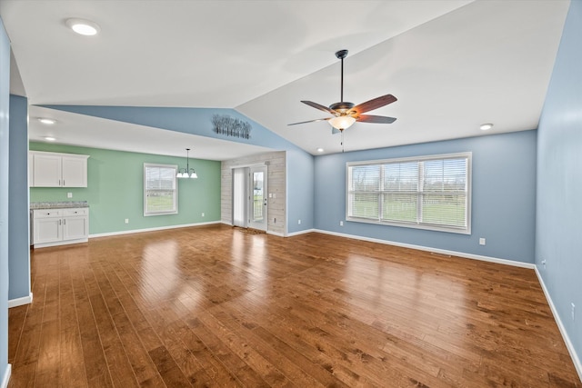 unfurnished living room with hardwood / wood-style flooring, ceiling fan with notable chandelier, baseboards, and lofted ceiling