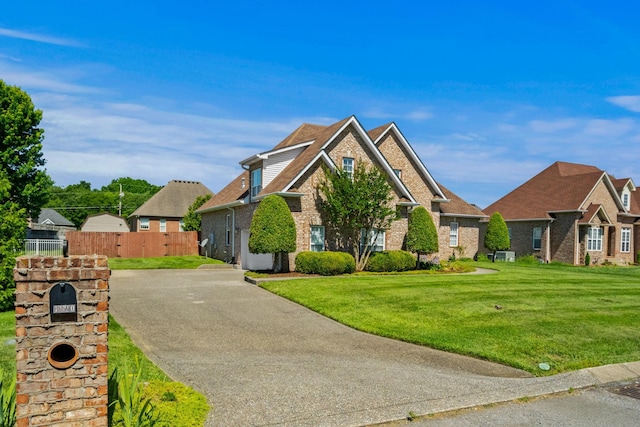 view of front facade with brick siding, driveway, a front yard, and fence