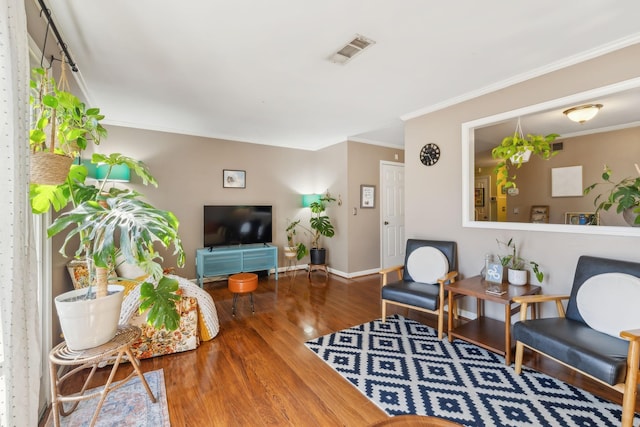 living room featuring visible vents, baseboards, wood finished floors, and crown molding