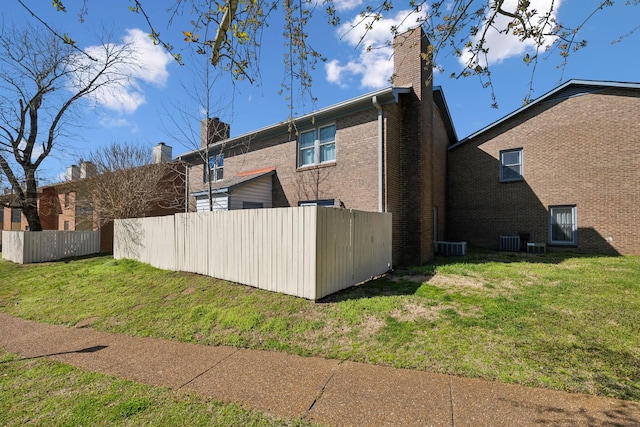 view of home's exterior with fence, cooling unit, a yard, brick siding, and a chimney
