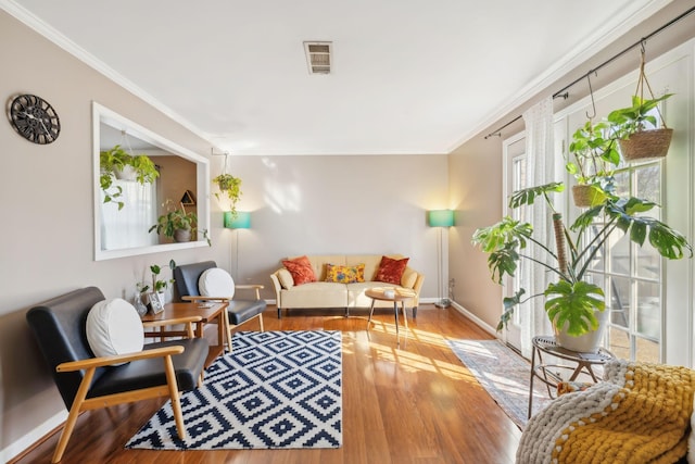 living room featuring visible vents, crown molding, baseboards, and wood finished floors