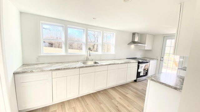 kitchen featuring light stone countertops, light wood-type flooring, electric range oven, wall chimney exhaust hood, and a sink