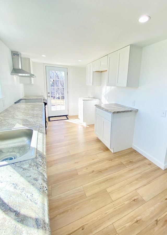 kitchen with white cabinetry, light wood-style flooring, wall chimney exhaust hood, and a sink