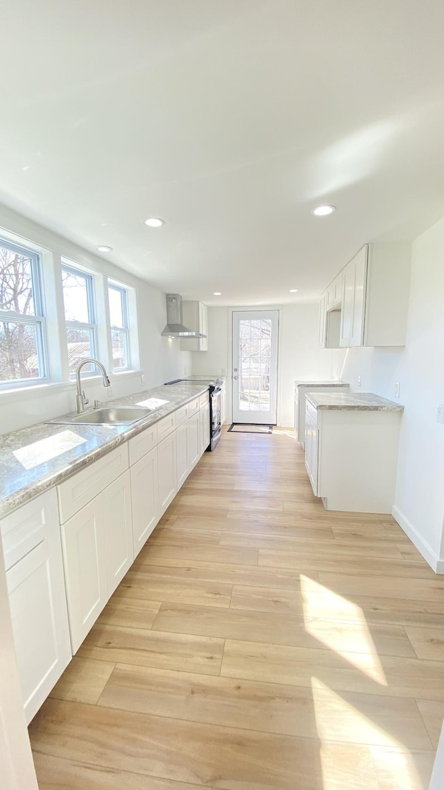 kitchen featuring white cabinets, wall chimney exhaust hood, light wood finished floors, and a sink