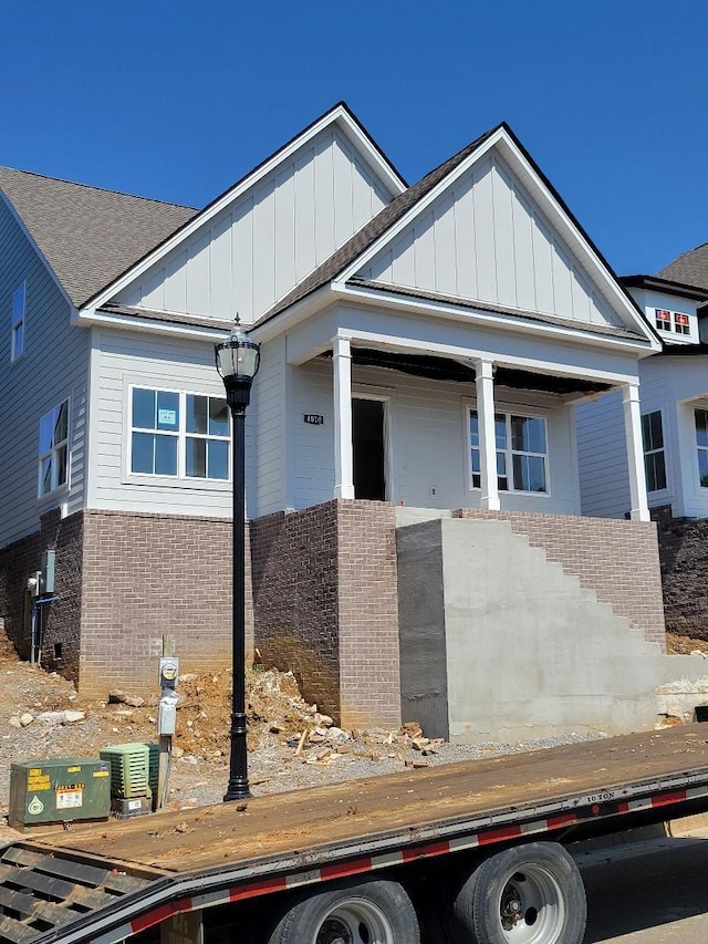 view of front of property with a shingled roof, board and batten siding, and brick siding