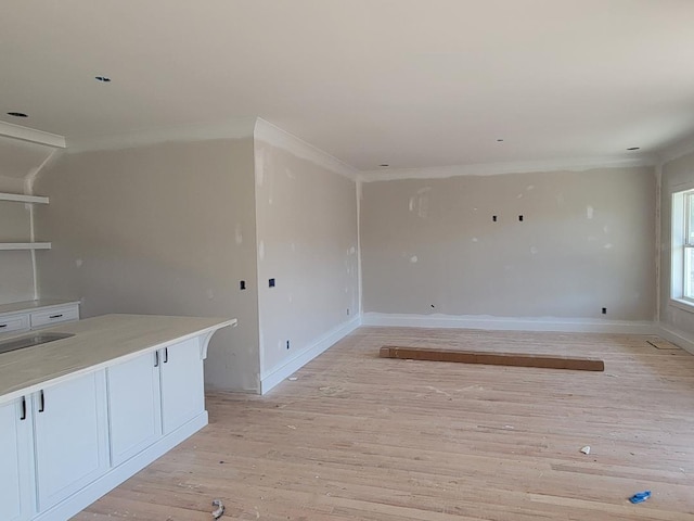 empty room with ornamental molding, light wood finished floors, a sink, and baseboards