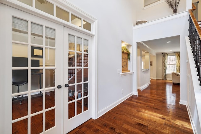 corridor featuring french doors, wood-type flooring, a high ceiling, baseboards, and stairs