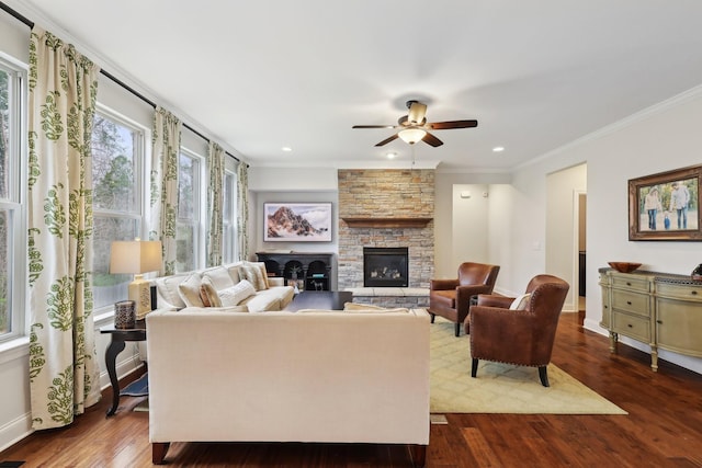 living area with dark wood-style floors, baseboards, ornamental molding, a stone fireplace, and ceiling fan