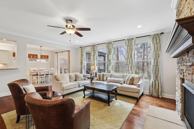 living room featuring a stone fireplace, baseboards, ceiling fan, and wood finished floors