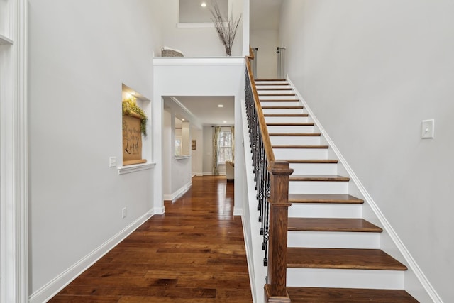 stairway featuring a high ceiling, wood finished floors, and baseboards
