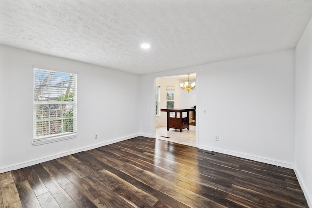 spare room with a notable chandelier, a textured ceiling, baseboards, and hardwood / wood-style floors