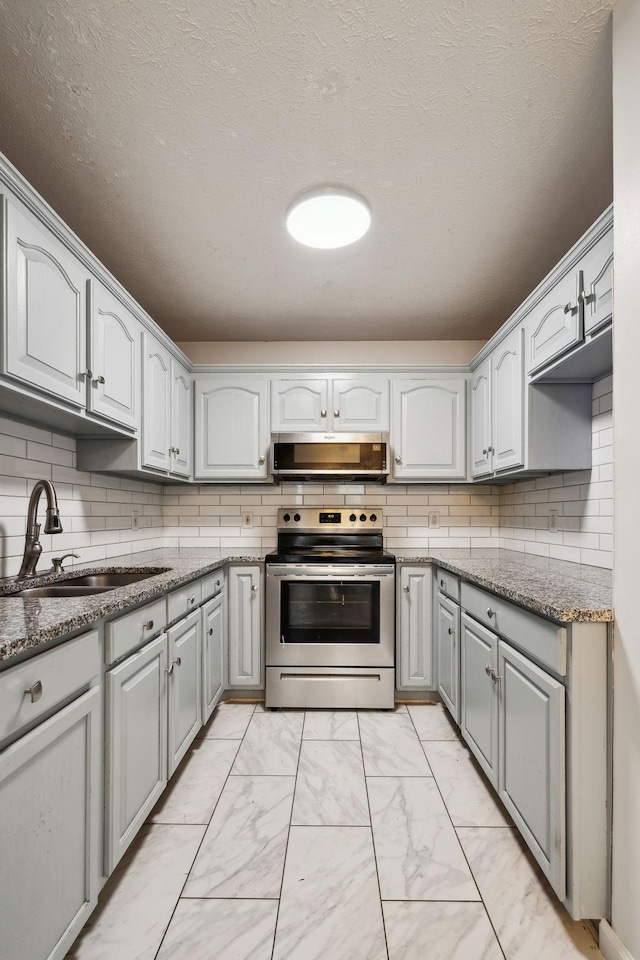 kitchen with a sink, gray cabinets, marble finish floor, and stainless steel appliances