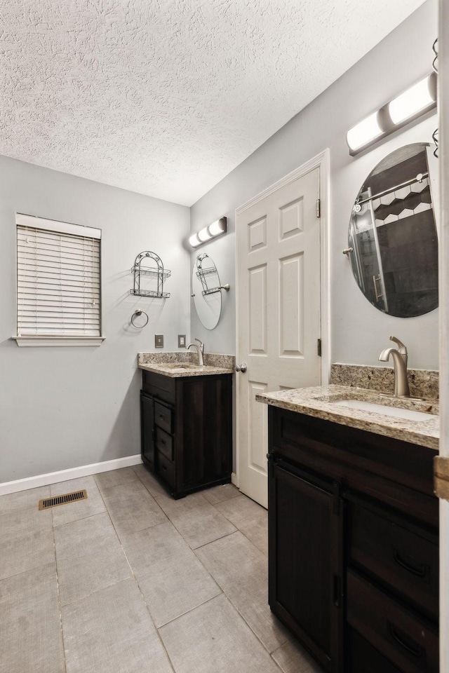 bathroom with visible vents, baseboards, tile patterned floors, a textured ceiling, and a sink