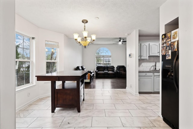 dining space with baseboards, a textured ceiling, and ceiling fan with notable chandelier