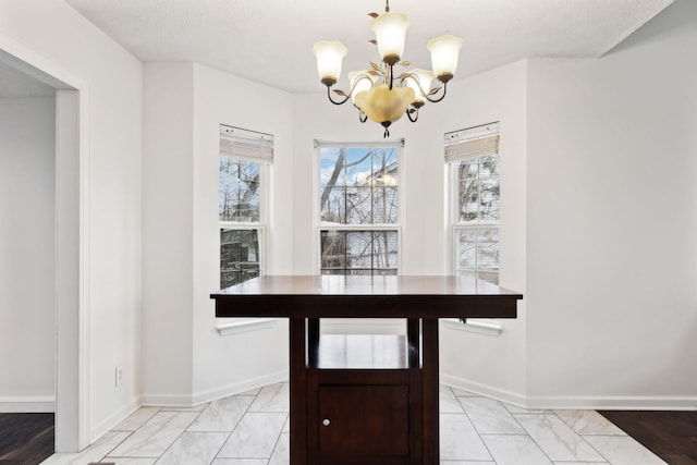 unfurnished dining area featuring a chandelier, marble finish floor, and baseboards