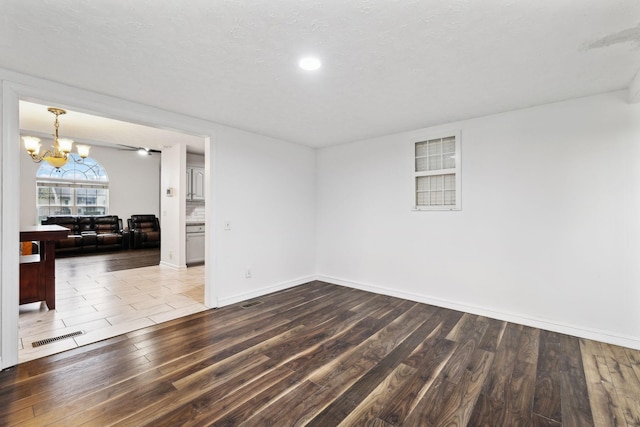 unfurnished room featuring visible vents, a textured ceiling, wood finished floors, an inviting chandelier, and baseboards