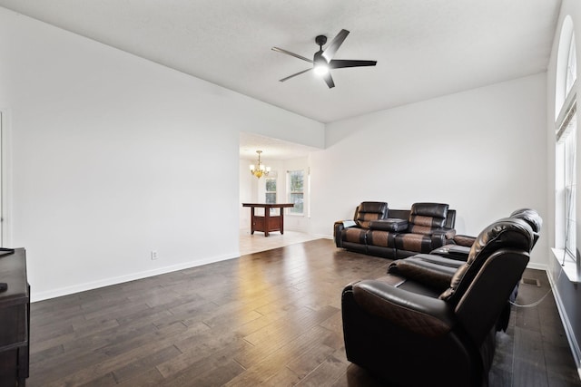 living area with ceiling fan with notable chandelier, dark wood-style flooring, and baseboards