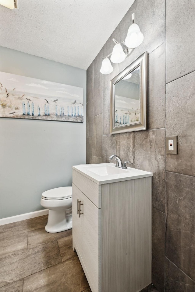 bathroom with vanity, baseboards, a textured ceiling, tile walls, and toilet