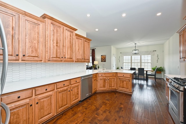 kitchen featuring appliances with stainless steel finishes, a peninsula, dark wood-style floors, decorative backsplash, and a sink