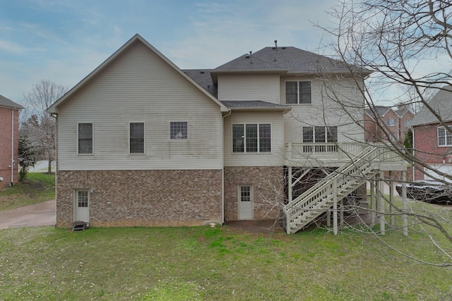 rear view of house featuring brick siding, a wooden deck, a lawn, and stairs