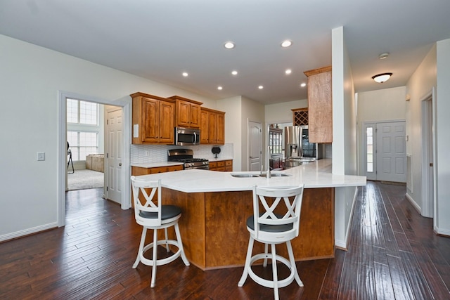 kitchen featuring brown cabinetry, dark wood-type flooring, appliances with stainless steel finishes, a sink, and decorative backsplash