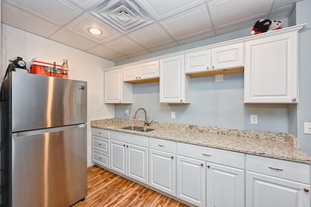 kitchen featuring light wood finished floors, a sink, freestanding refrigerator, and white cabinetry