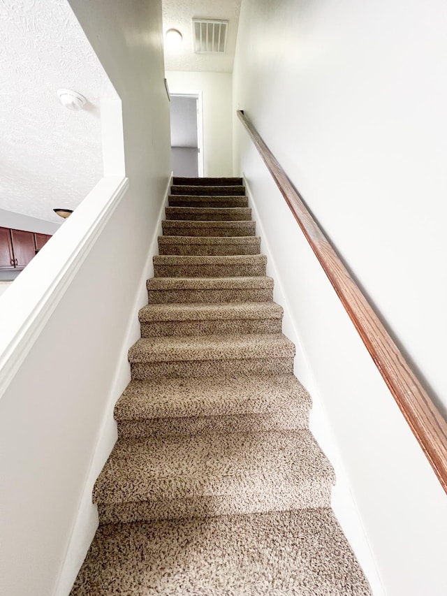 stairway with visible vents and a textured ceiling