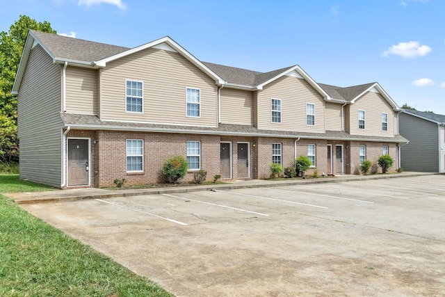 multi unit property featuring brick siding, uncovered parking, and roof with shingles