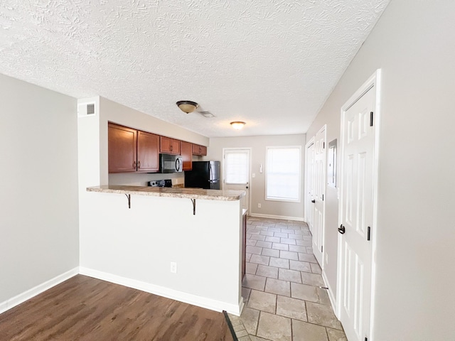 kitchen featuring visible vents, brown cabinets, black appliances, a peninsula, and a breakfast bar area