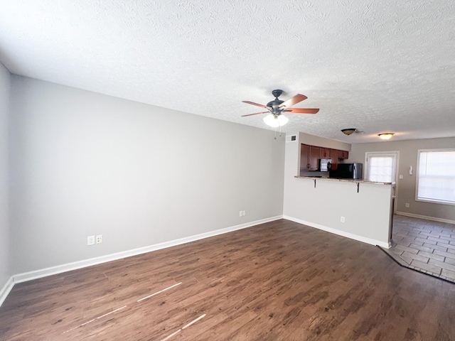 unfurnished living room featuring a ceiling fan, visible vents, baseboards, dark wood finished floors, and a textured ceiling