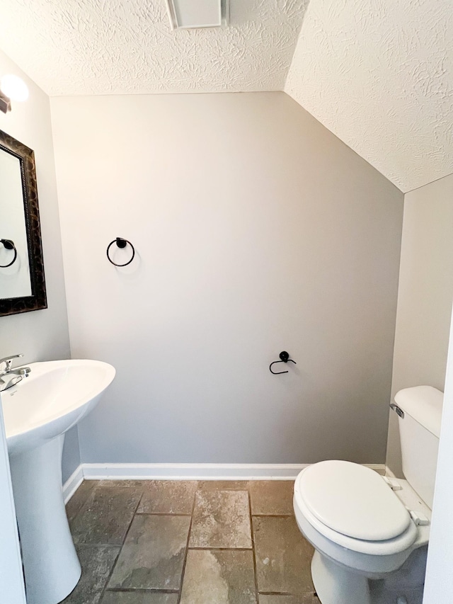 bathroom with a textured ceiling, toilet, baseboards, and vaulted ceiling