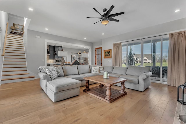 living room with recessed lighting, ceiling fan with notable chandelier, stairs, and light wood finished floors