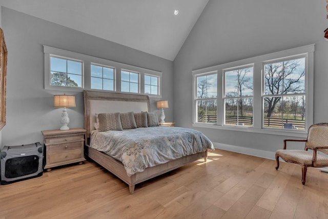 bedroom with light wood finished floors, high vaulted ceiling, and baseboards
