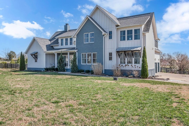 modern farmhouse style home with driveway, fence, board and batten siding, a front yard, and a chimney