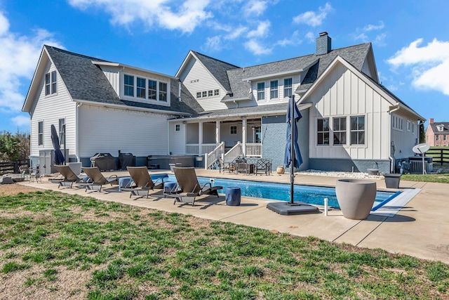 back of house with roof with shingles, an outdoor pool, a lawn, a patio area, and board and batten siding