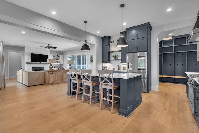 kitchen featuring light wood-style flooring, stainless steel appliances, a breakfast bar area, light countertops, and ceiling fan