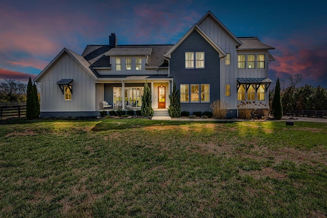 back of property at dusk featuring a lawn, board and batten siding, a chimney, and fence