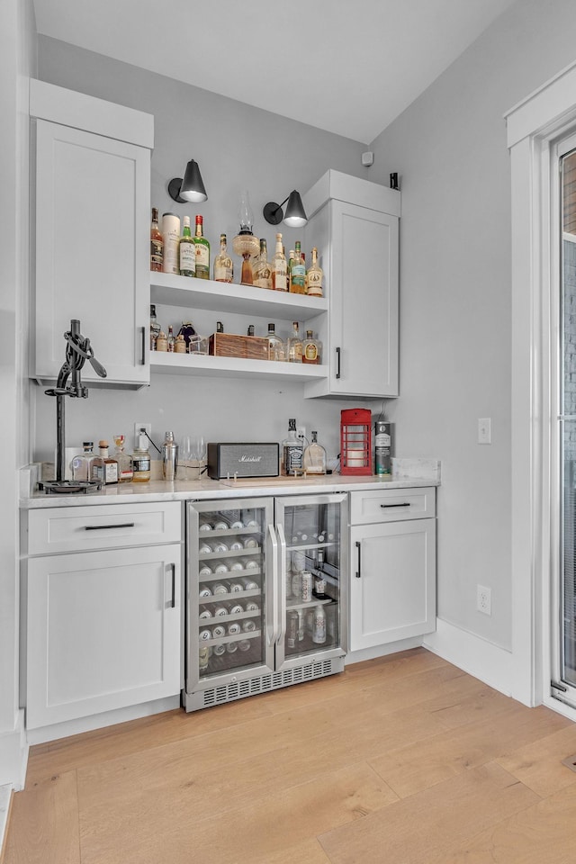 bar featuring wine cooler, a bar, light wood-type flooring, and baseboards