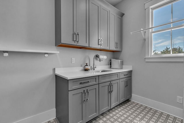 clothes washing area with a sink, baseboards, and light floors