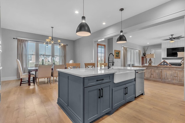 kitchen with light wood finished floors, gray cabinetry, light countertops, stainless steel dishwasher, and a sink