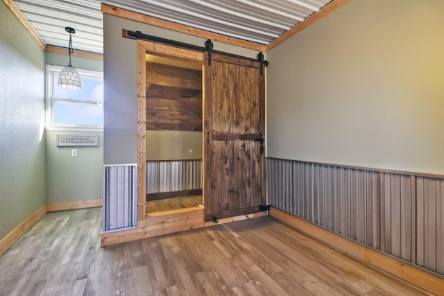 unfurnished room featuring a barn door, wood finished floors, and baseboards