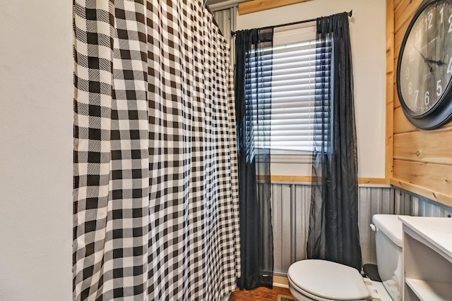 full bathroom with curtained shower, toilet, and wainscoting