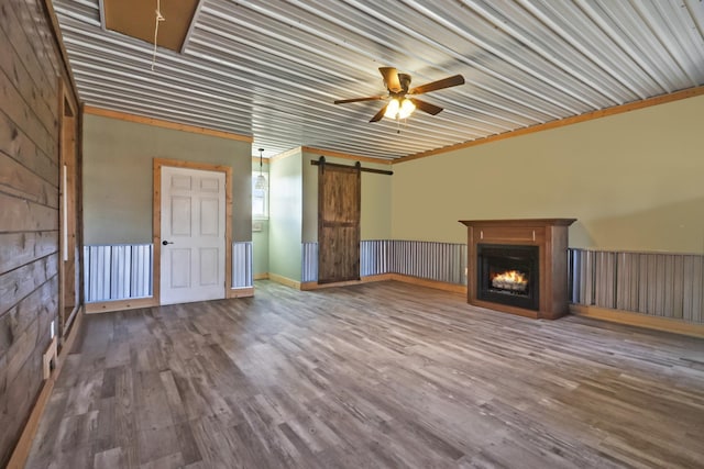 unfurnished living room with a ceiling fan, a warm lit fireplace, wood finished floors, a barn door, and attic access